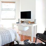 Bright dorm room with white walls, a window, partial view of the bed, and a desk, PC and chair.