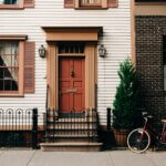 rowhouses with red front down and black iron fence, and a bike leaning against it.