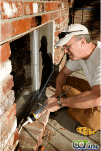 Person caulking a window to reduce energy loss.